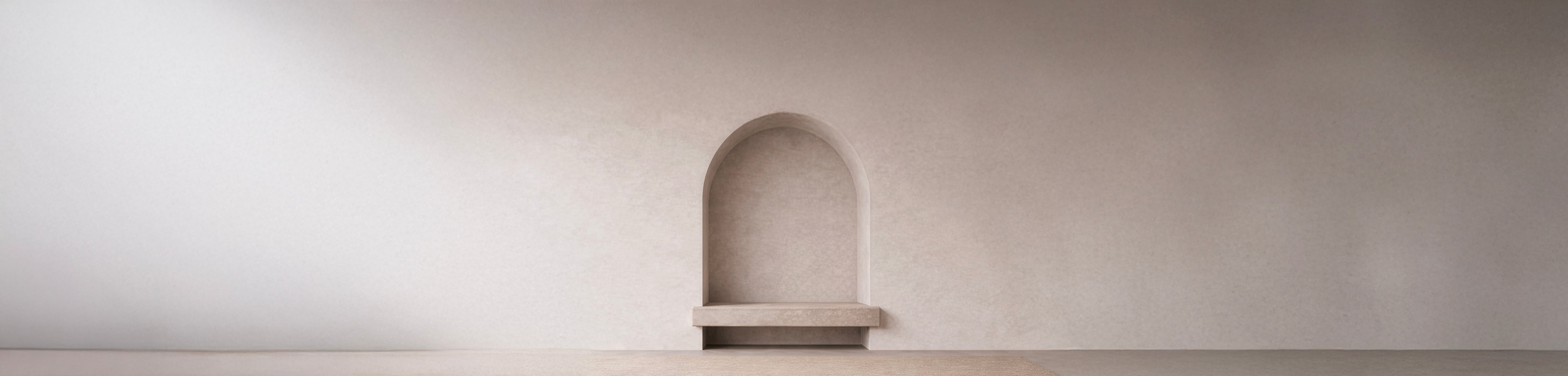 Empty arched wall niche in warm off-white plaster with a stone bench shelf, softly lit above a woven neutral floor.