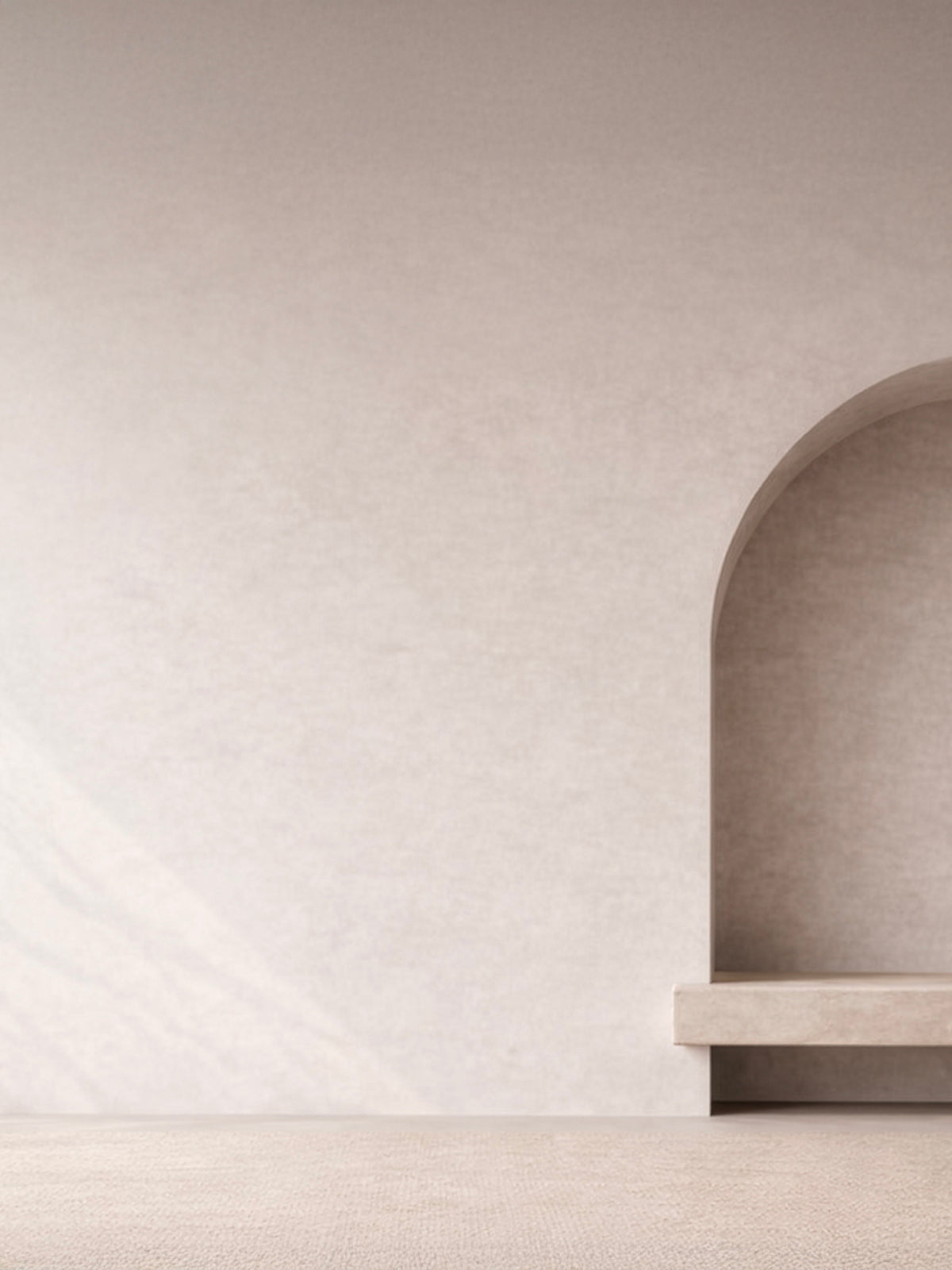 Empty arched wall niche in warm off-white plaster with a stone bench shelf, softly lit above a woven neutral floor.